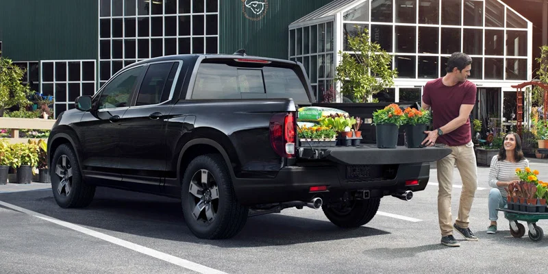 A person loading new potted plants into the bed of their 2025 Honda Ridgeline near Orangeburg, SC